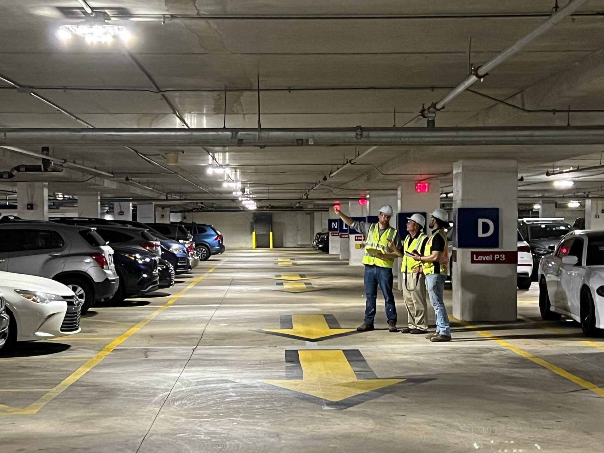 Three men in yellow vests inspecting a full parking garage